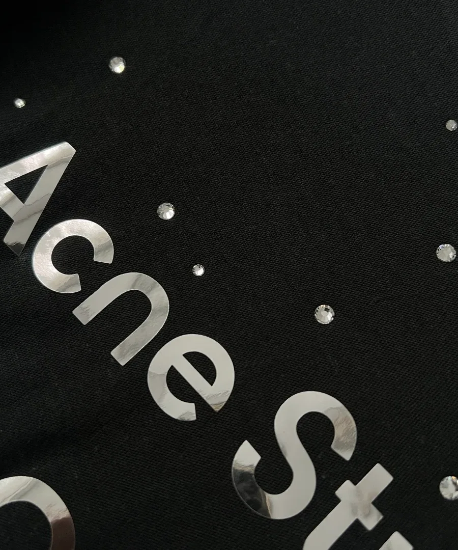 Макроплан надписи Acne Studios из глянцевой зеркальной плёнки и термостраз