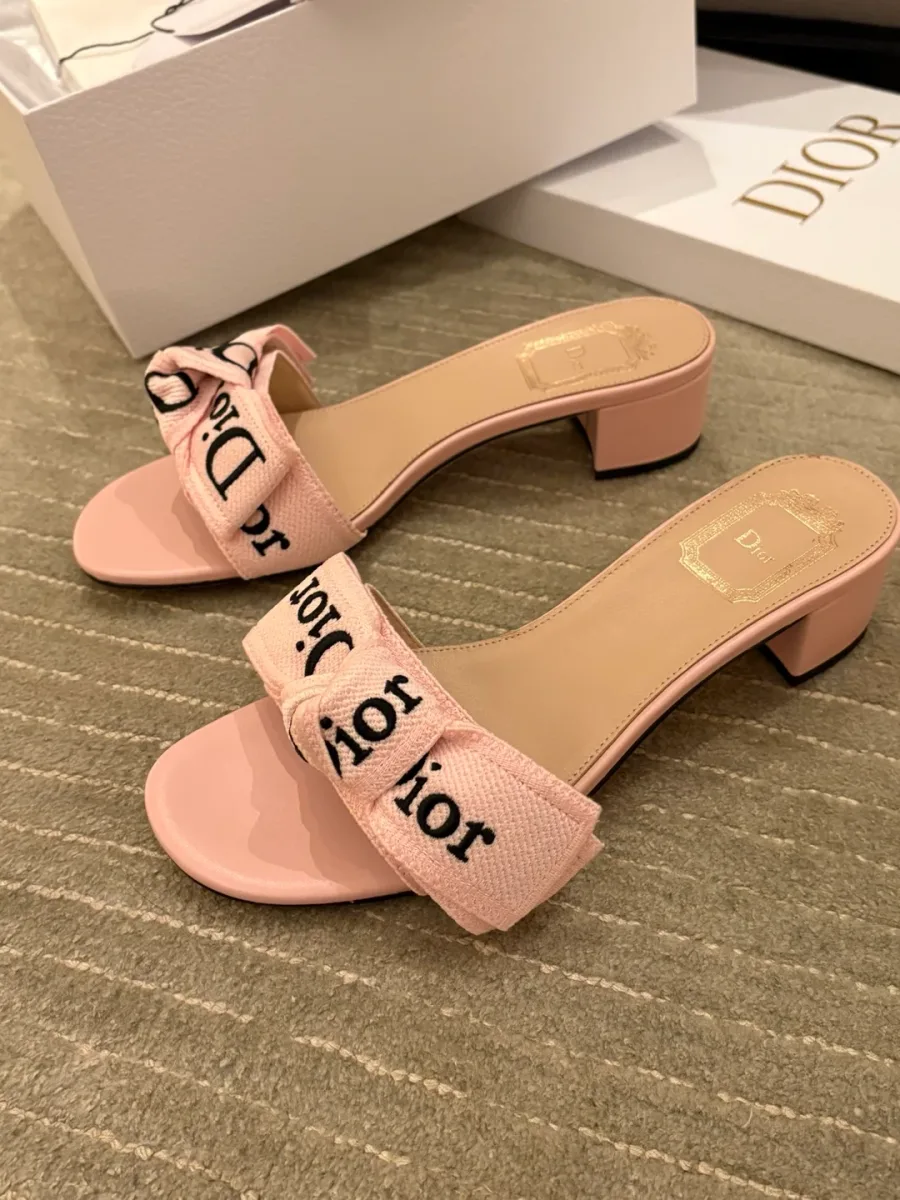 Пара розовых шлёпанцев с текстильным бантом и логотипом Dior на светлом фоне