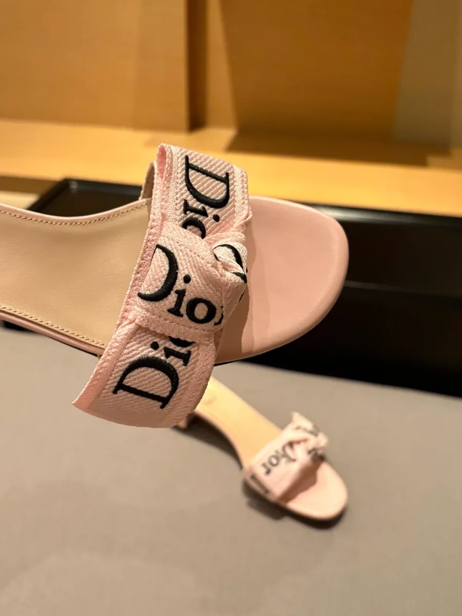 Крупный план текстильного ремешка с бантом и вышивкой Dior на розовом шлёпанце