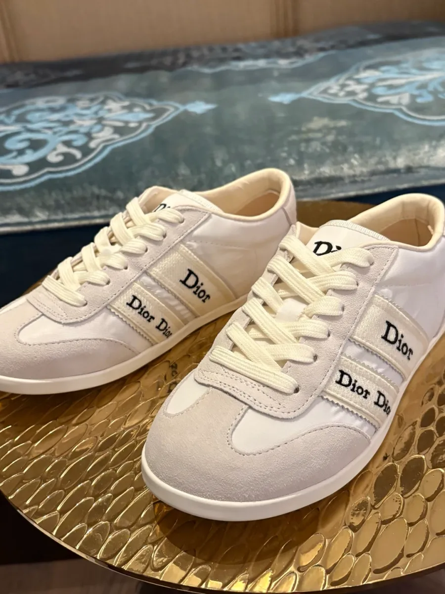 Кроссовки белого цвета с полосами Dior на золотистом столике, вид спереди три четверти