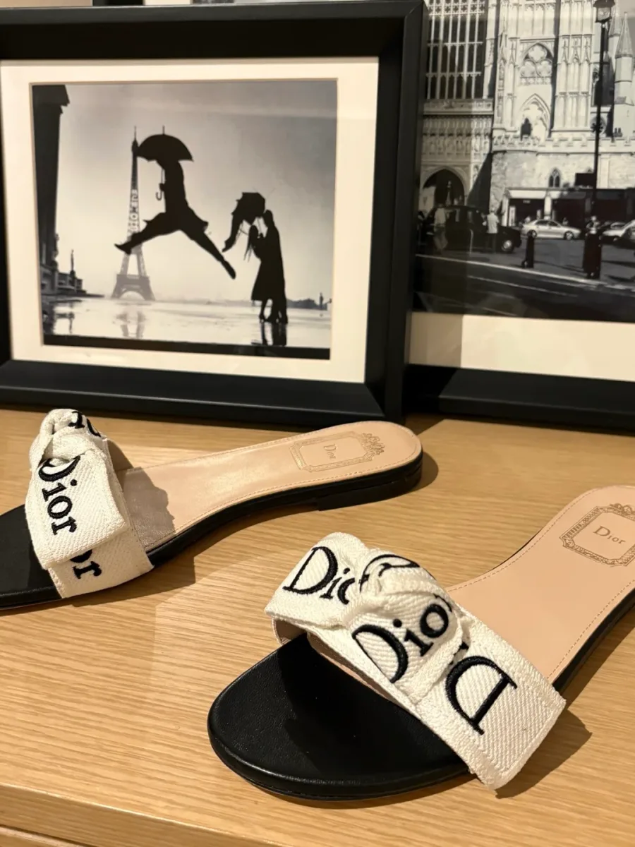 Пара шлепанцев с бантом Dior на фоне интерьерных фоторамок