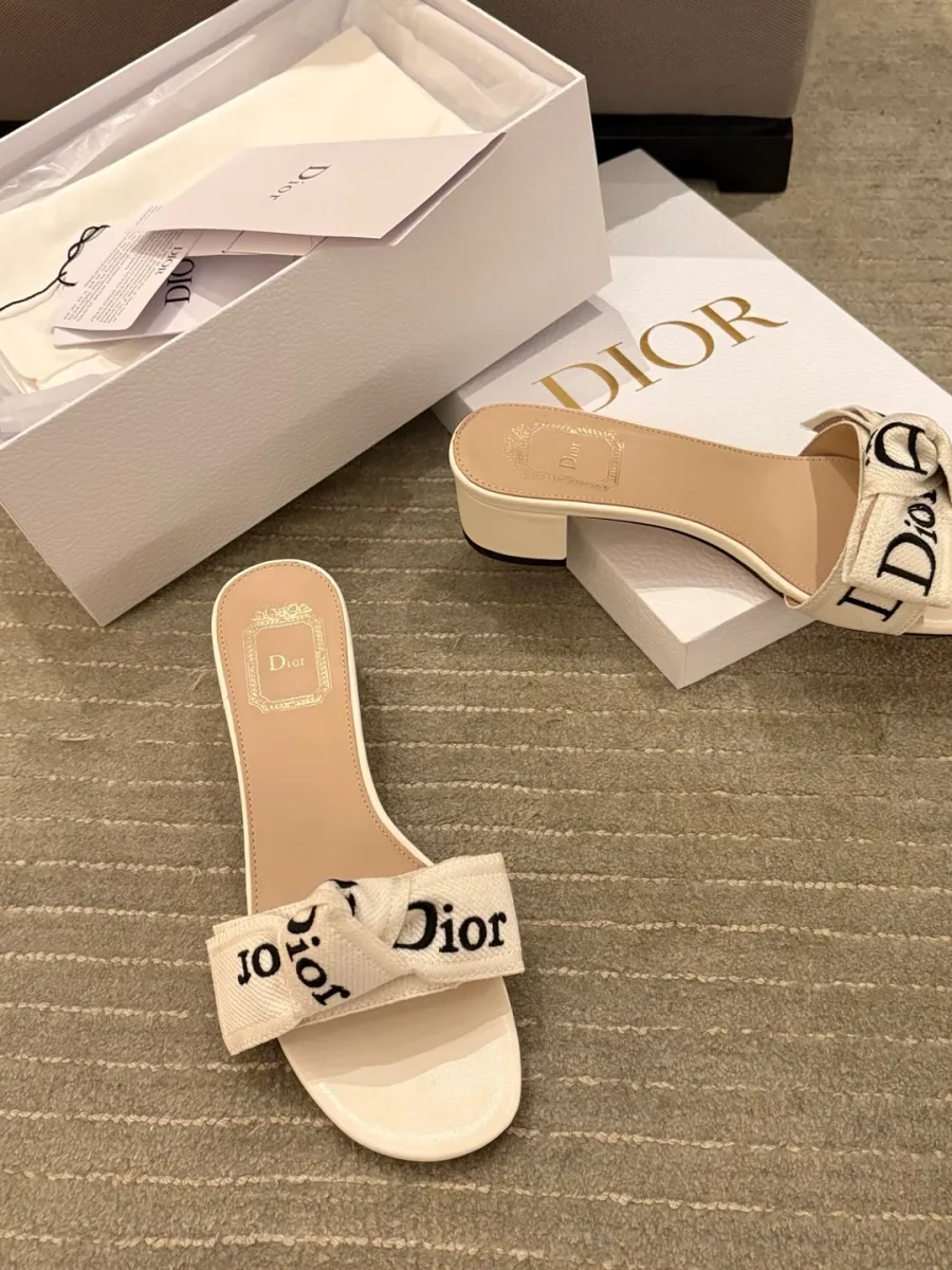 Белые шлёпанцы на каблуке с бантом и вышивкой Dior на фоне фирменной коробки, вид сверху