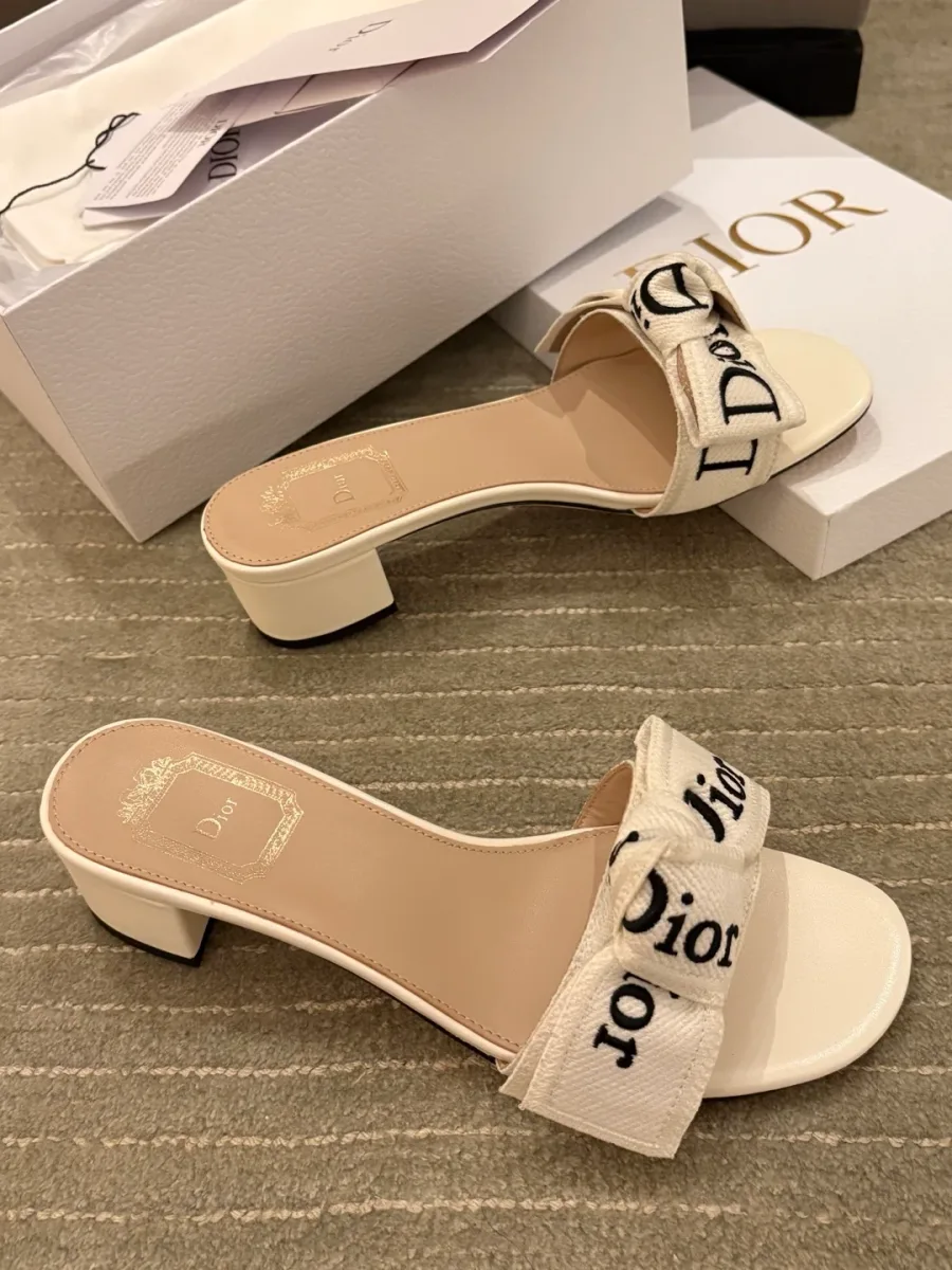 Пара белых шлёпанцев на каблуке с вышивкой Dior на фоне коробки, вид сбоку