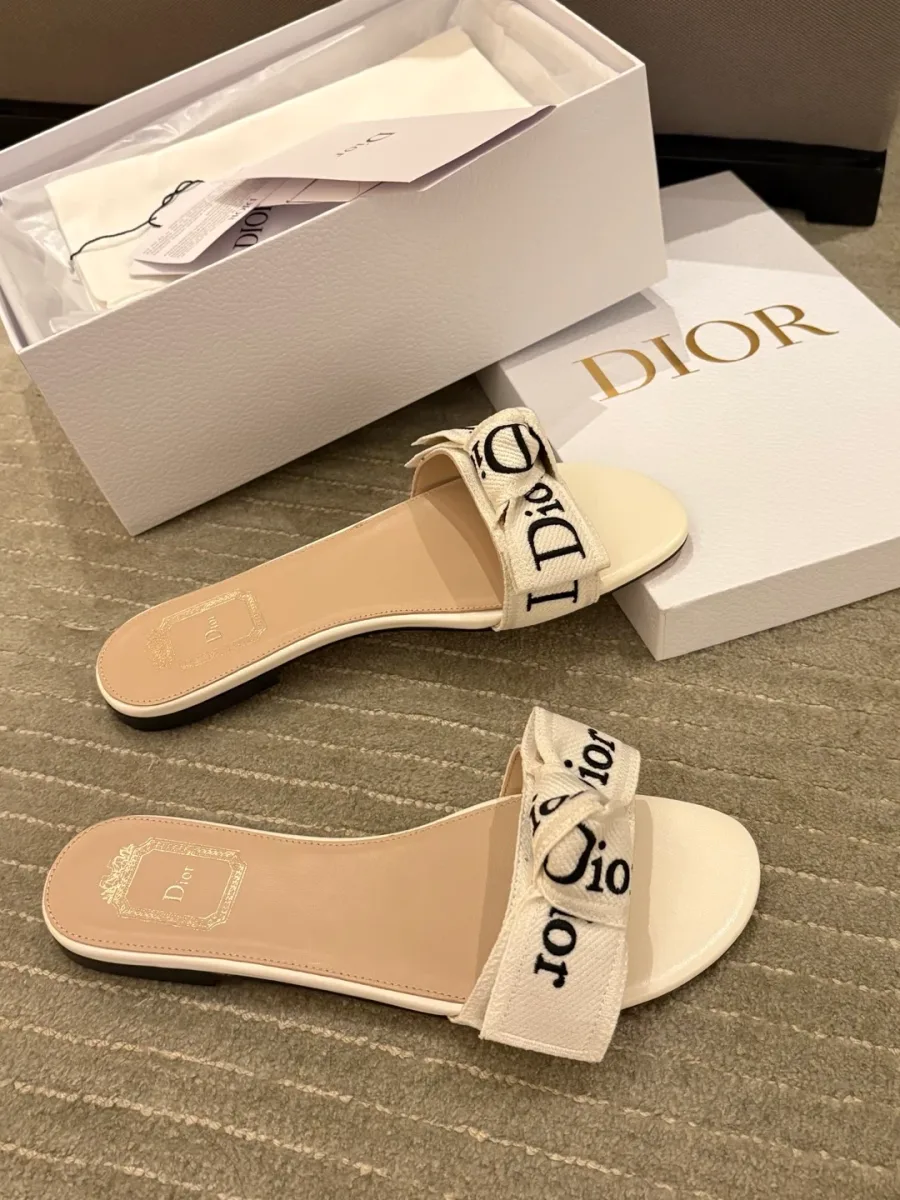 Пара белых шлёпанцев Dior с вышитым бантом около коробки
