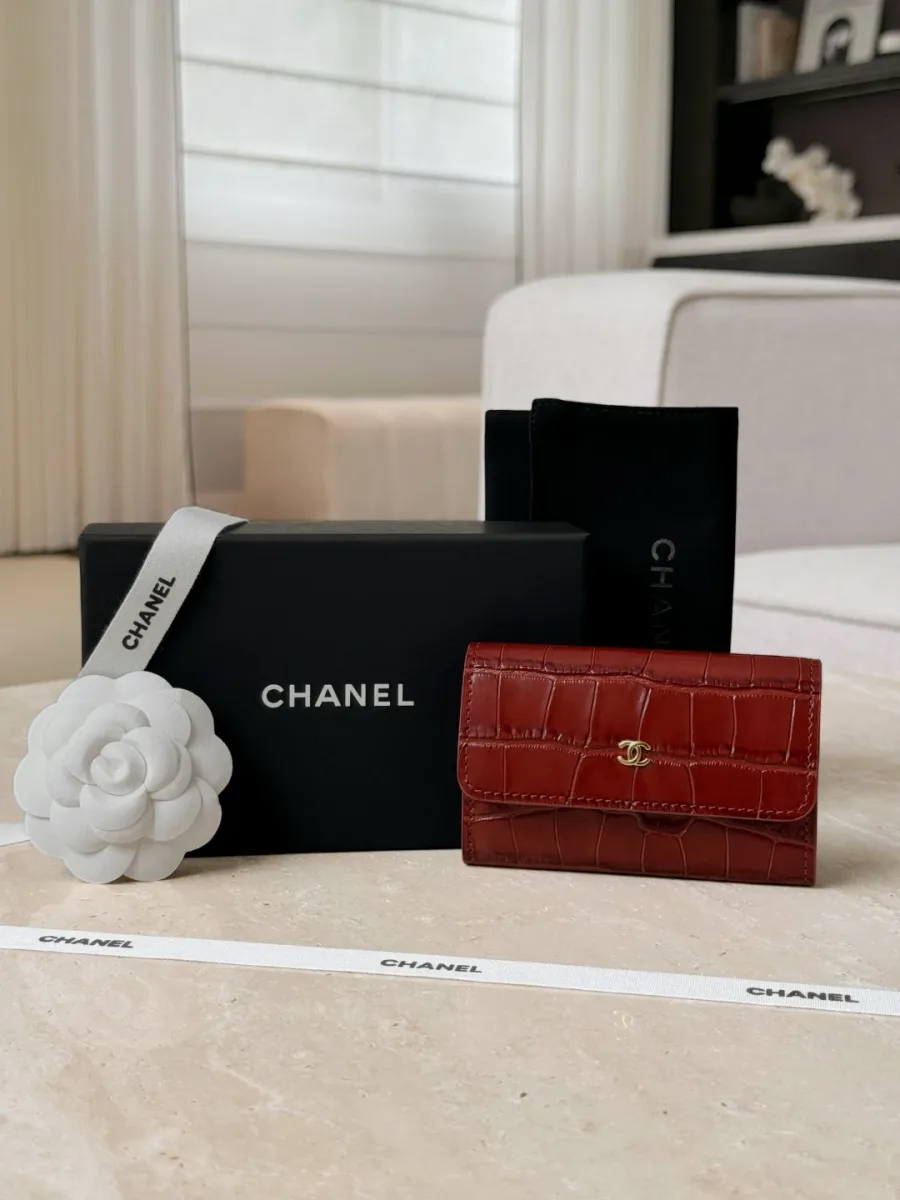 Бордовый картхолдер Chanel рядом с фирменной коробкой, лентой и цветком камелии