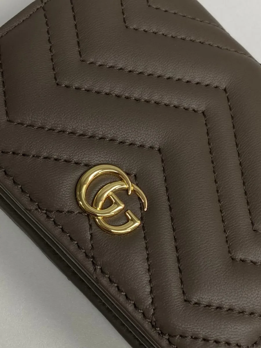 Крупный план золотистой металлической эмблемы Double G и фактурной стеганой кожи