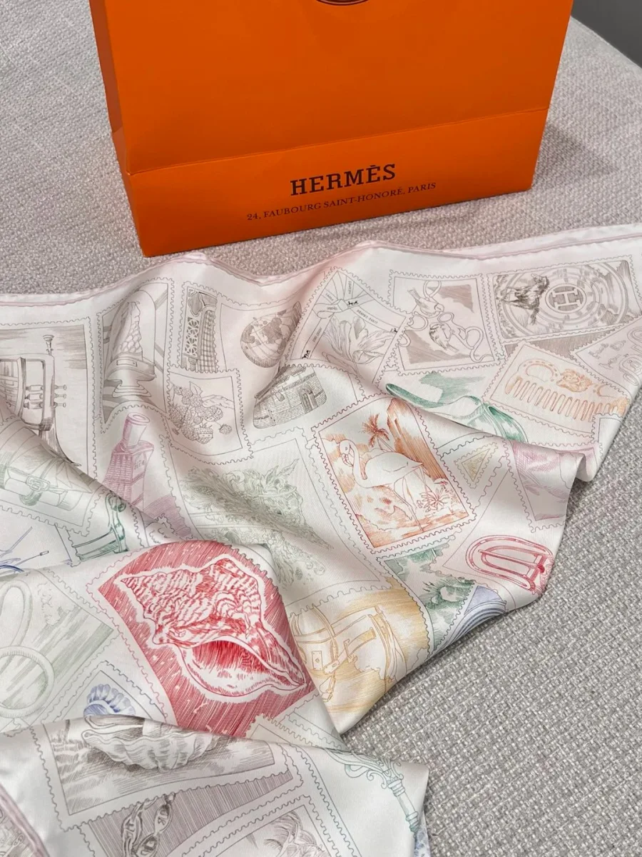 Сложенный платок Hermes с рисунком марок рядом с фирменным пакетом