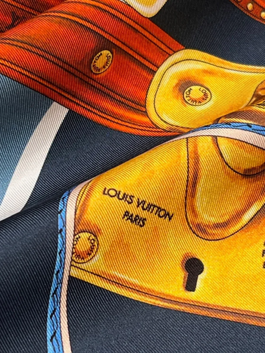 Деталь шёлковой ткани с принтом чемоданного замка и надписью Louis Vuitton Paris Maison Fondée En 1854
