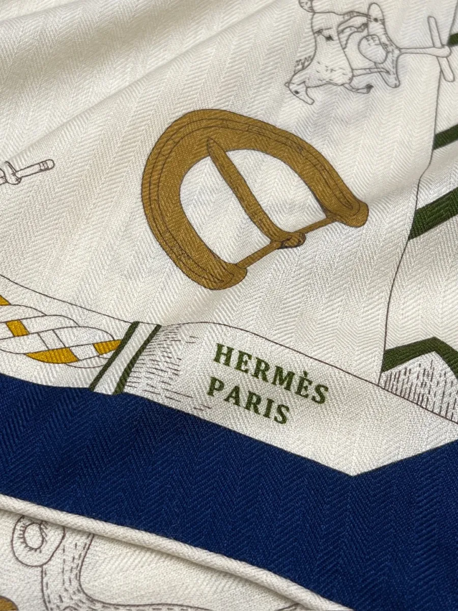 Крупный план угла шали с надписью Hermes Paris, пряжкой и синей каймой