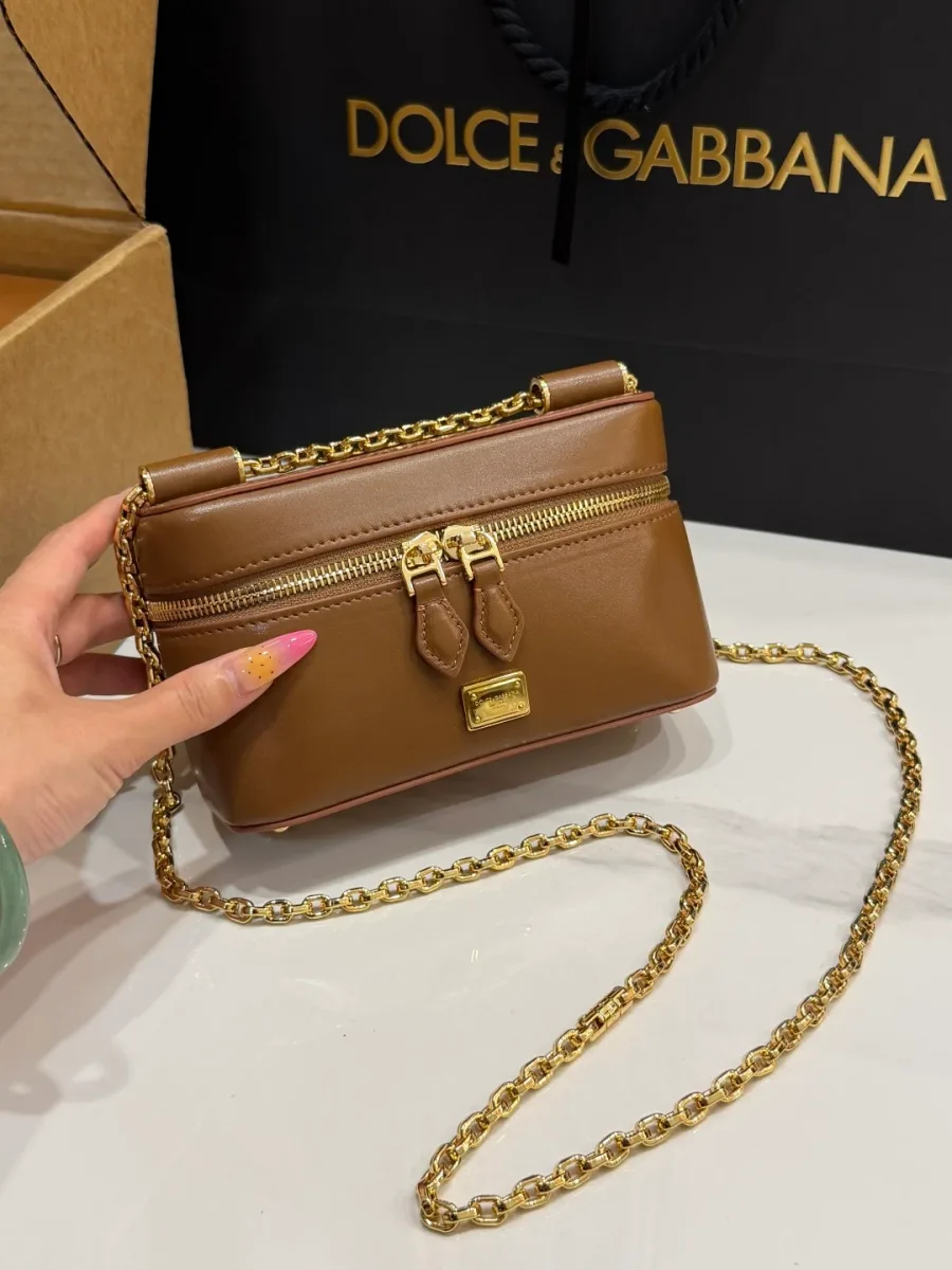 Коричневая сумка-косметичка Dolce & Gabbana Sicily в руке, вид спереди с золотистой табличкой