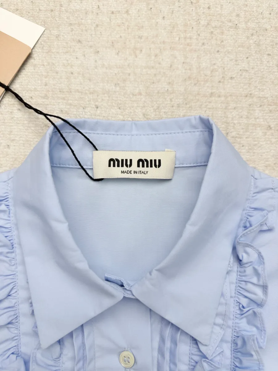 Отложной воротник и фирменная бирка Miu Miu на голубой рубашке крупным планом