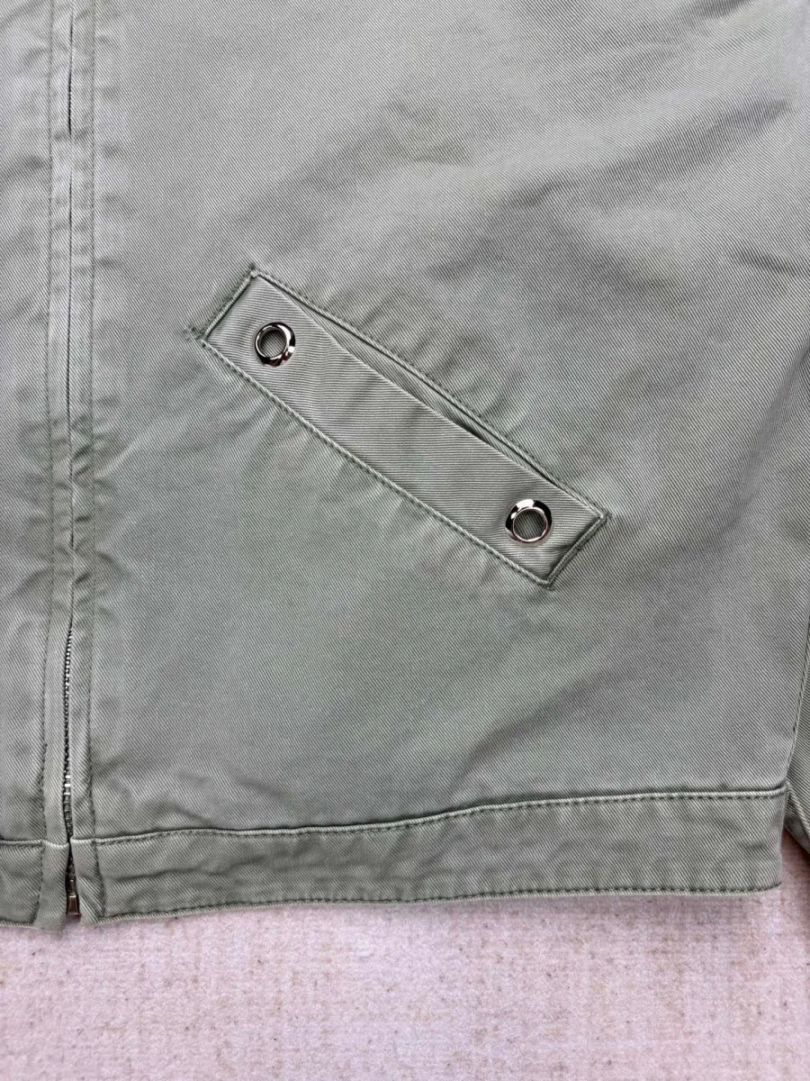 Прорезной карман с отделкой металлическими люверсами на серо-зелёной куртке