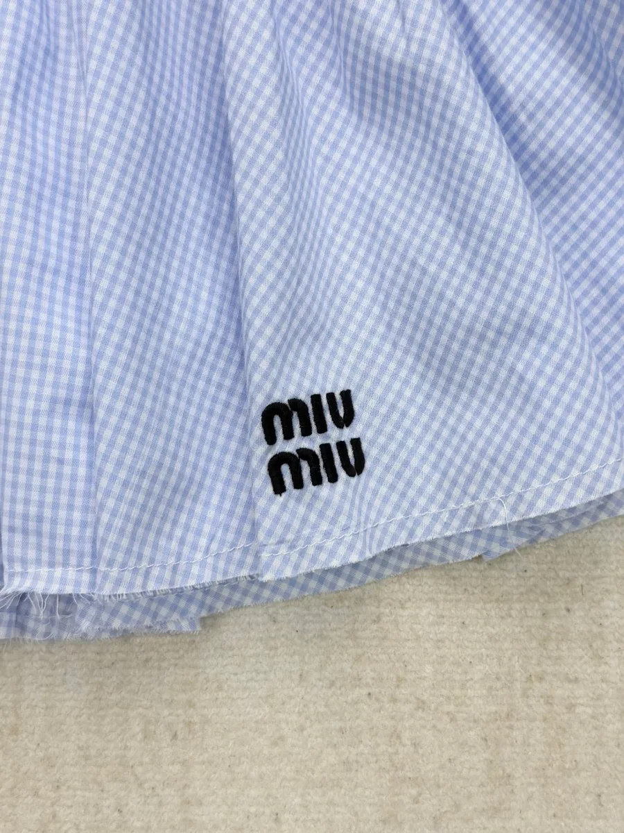 Вышитый черный логотип Miu Miu на подоле клетчатой юбки, деталь