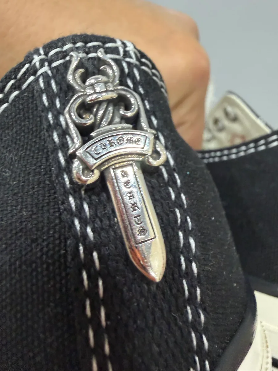 Крупный план серебряного декоративного кинжала Chrome Hearts на заднике кед