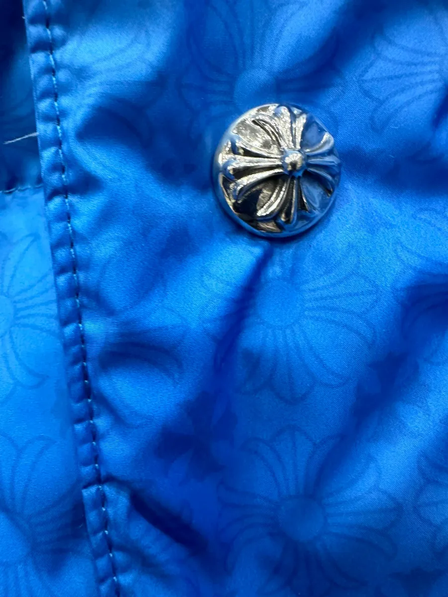 Деталь синего пуховика Chrome Hearts: серебряная кнопка с гравировкой