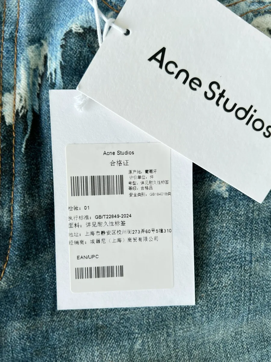 Фирменная бирка Acne Studios на фоне синей джинсовой ткани