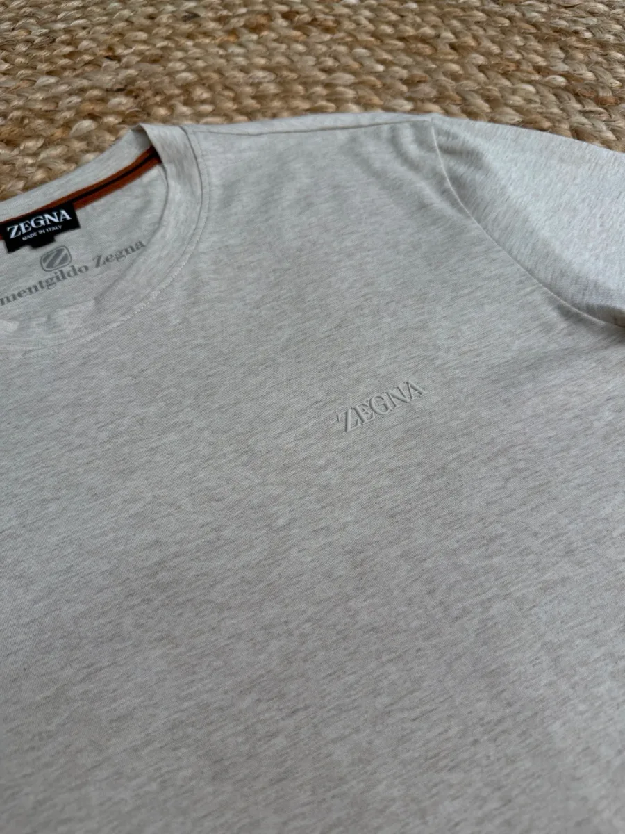 Тональная вышивка логотипа Zegna на груди светло-бежевой футболки крупным планом.