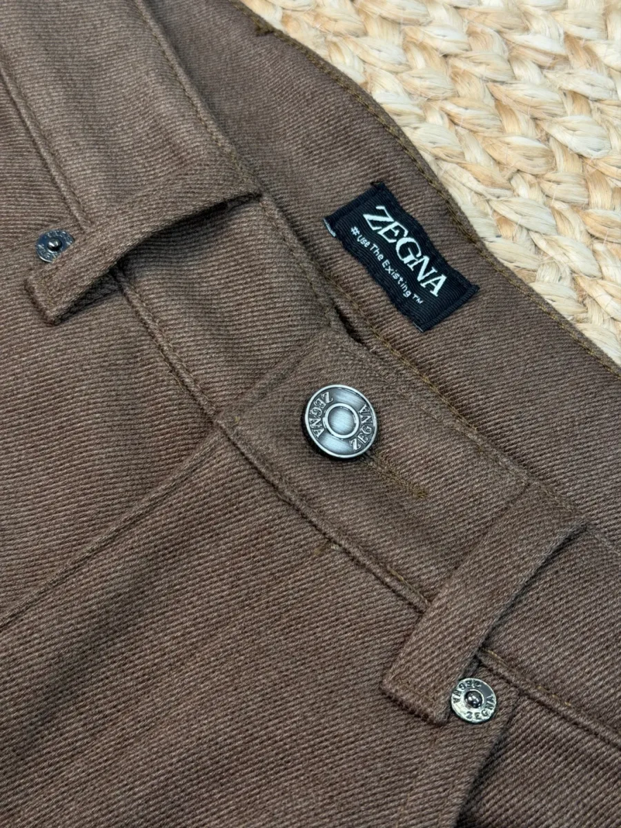 Крупный план пояса коричневых джинсов с металлической пуговицей Zegna, тканевым ярлыком и заклёпкой