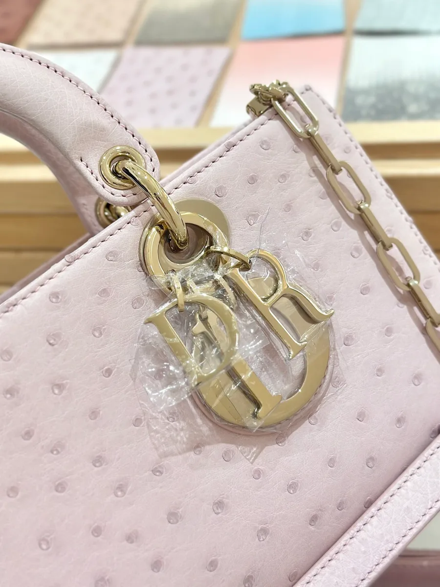Золотистая подвеска-шарм с буквами DIOR на розовой кожаной сумке