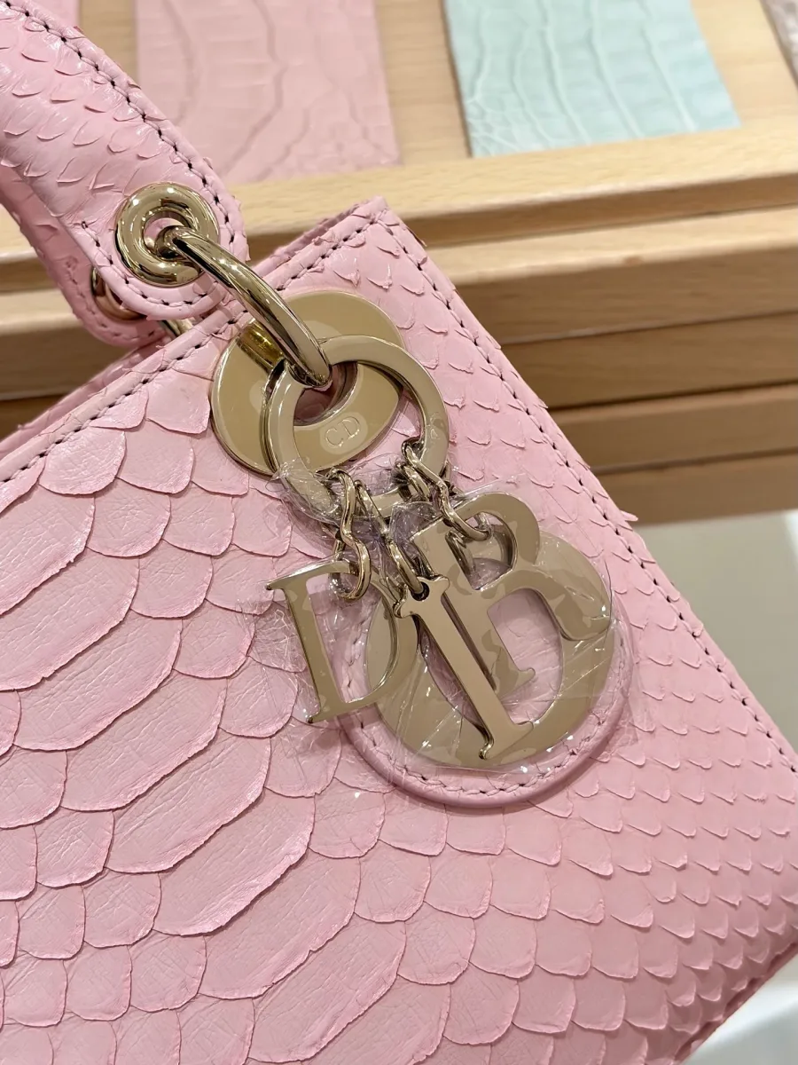 Крупный план золотистой подвески-шарма DIOR на розовой змеиной коже