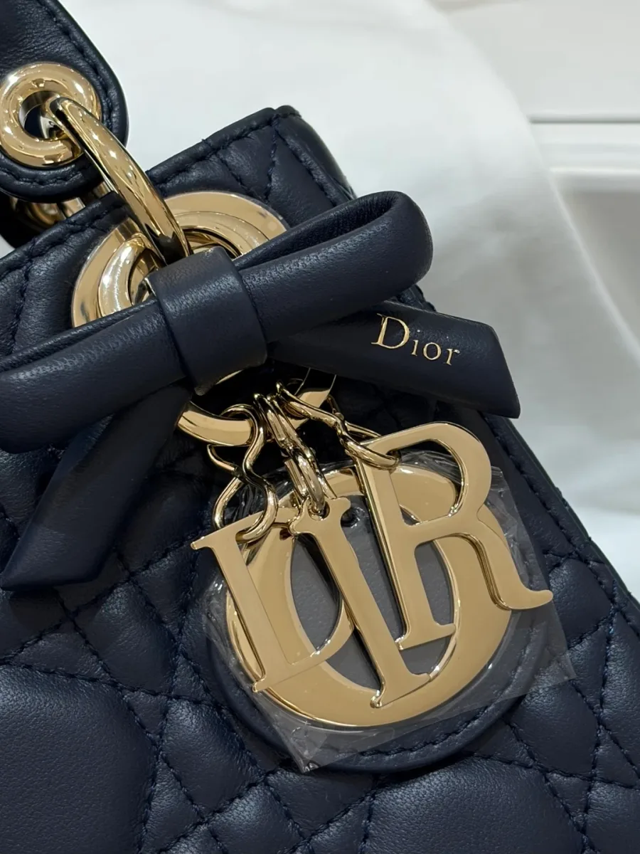 Крупный план золотистой подвески-логотипа DIOR с кожаным бантом на темно-синей сумке
