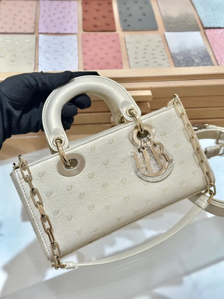 Бежево-золотая сумка Dior Lady D-Joy из кожи страуса в руке, вид спереди с подвеской DIOR