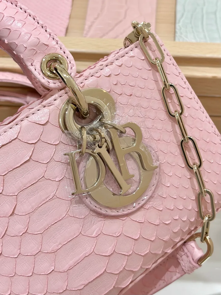 Крупный план золотистой подвески DIOR на розовой сумке из змеиной кожи