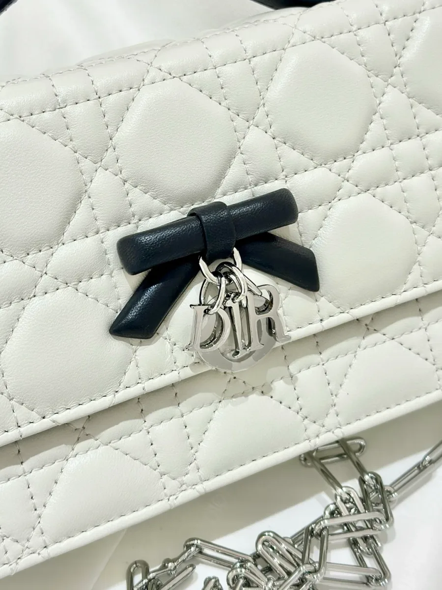 Крупный план черного кожаного банта с серебристой подвеской DIOR на белой сумке