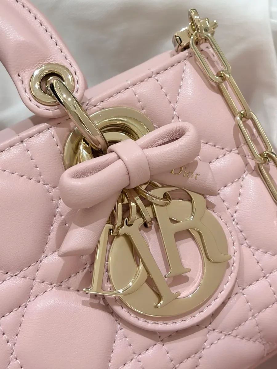 Крупный план подвески с буквами DIOR и декоративным бантом на розовой сумке