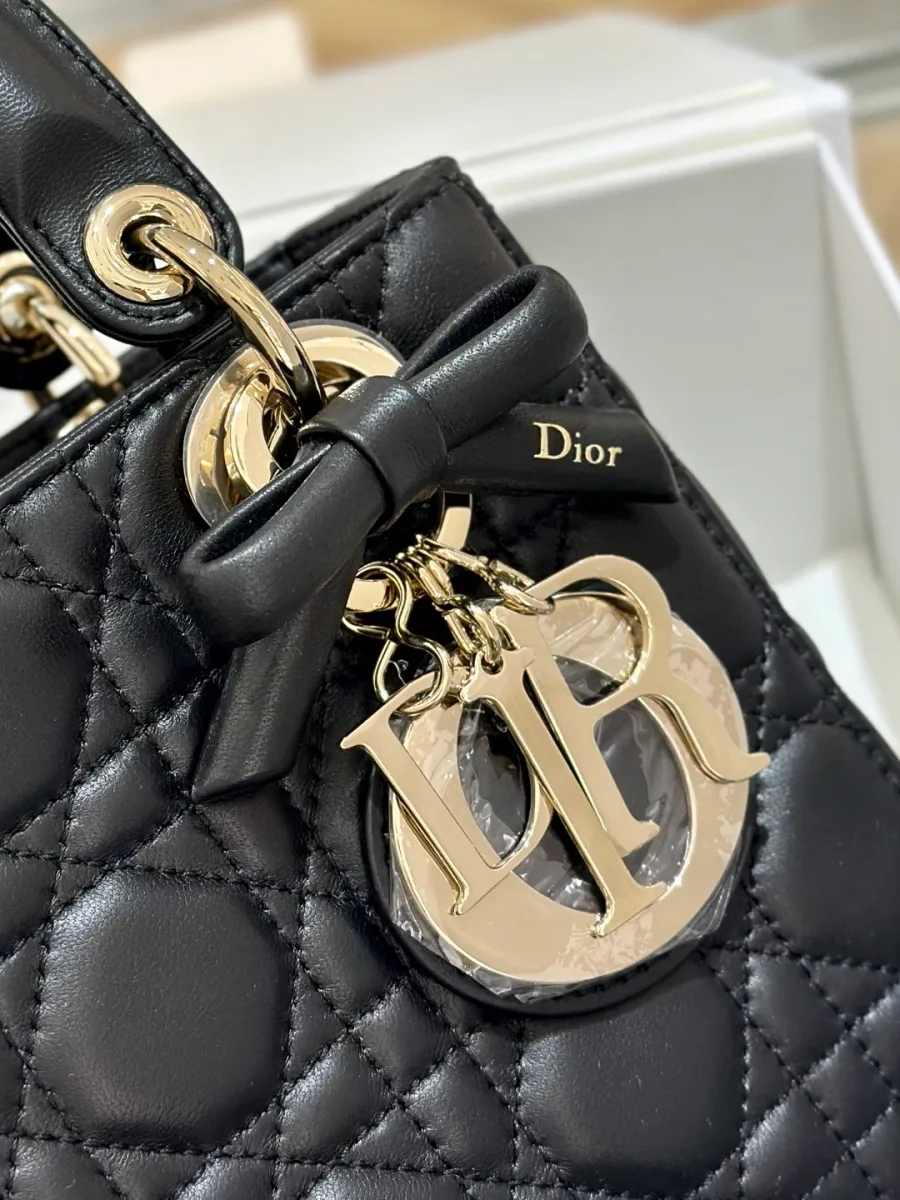 Крупный план золотистой подвески DIOR и кожаного банта на ручке сумки