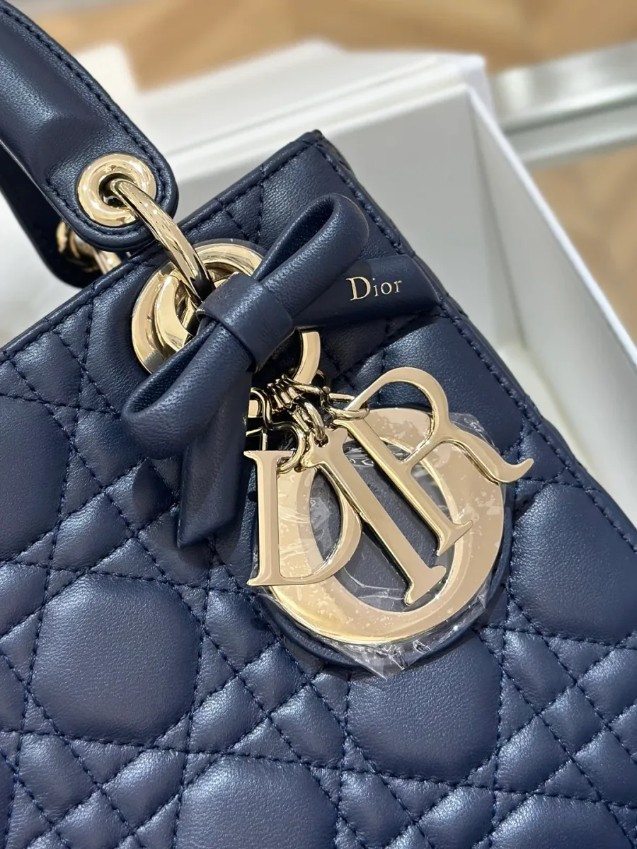 Крупный план золотистой подвески DIOR и кожаного банта на синей сумке