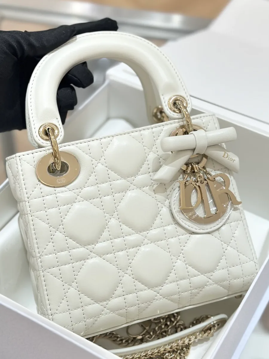 Белая стеганая сумка Dior Lady 17 с золотистой фурнитурой и декоративным бантом в руке