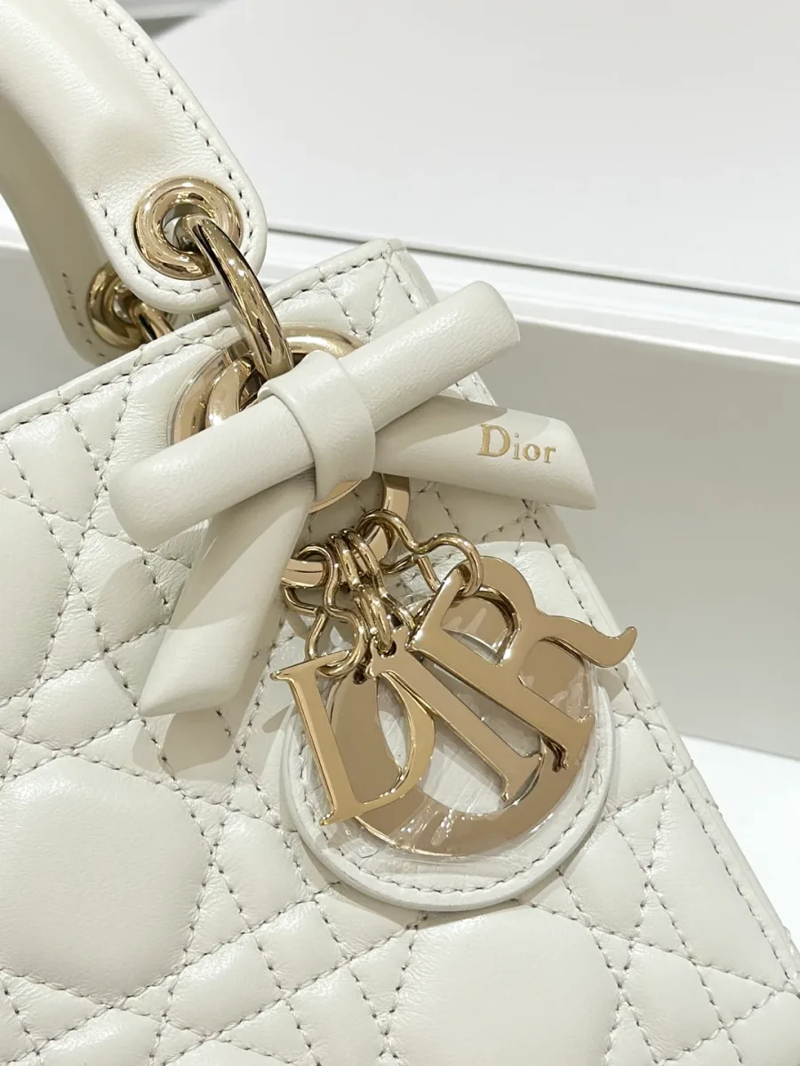 Крупный план золотистой подвески DIOR и кожаного банта на сумке