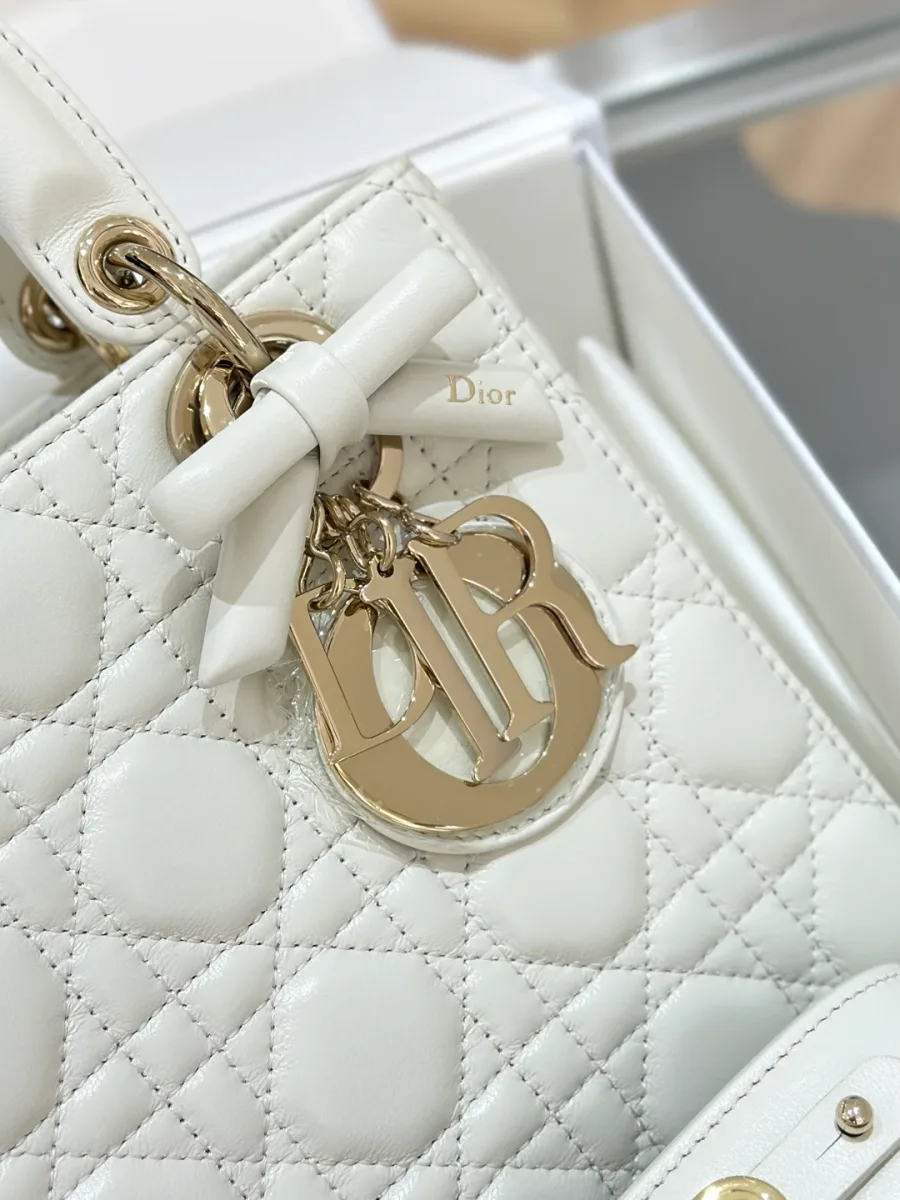 Крупный план золотистой подвески DIOR с декоративным бантом на белой сумке