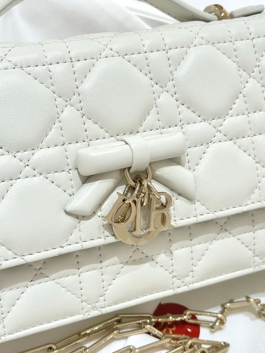 Крупный план клапана белой сумки с бантом и подвеской DIOR
