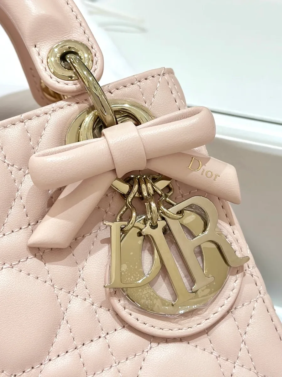 Крупный план золотистой подвески DIOR и кожаного банта на розовой сумке