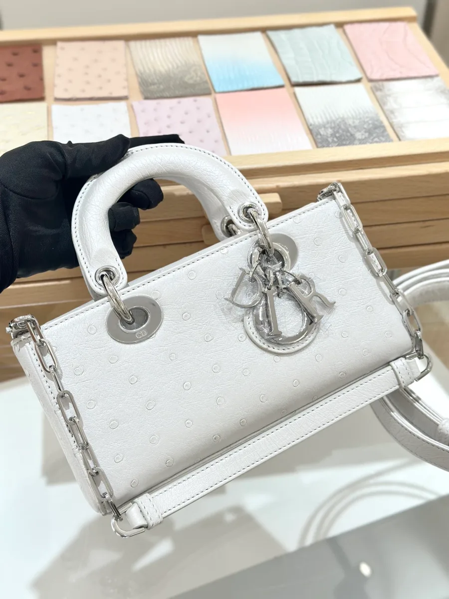 Белая сумка Dior Lady D-Joy 22 из кожи страуса в руке, вид спереди с подвеской DIOR