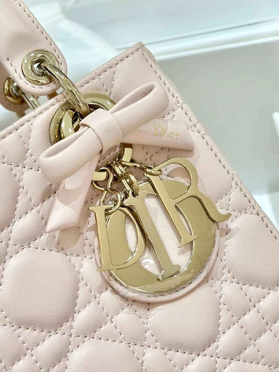 Крупный план золотистой подвески DIOR с кожаным бантом на розовой сумке