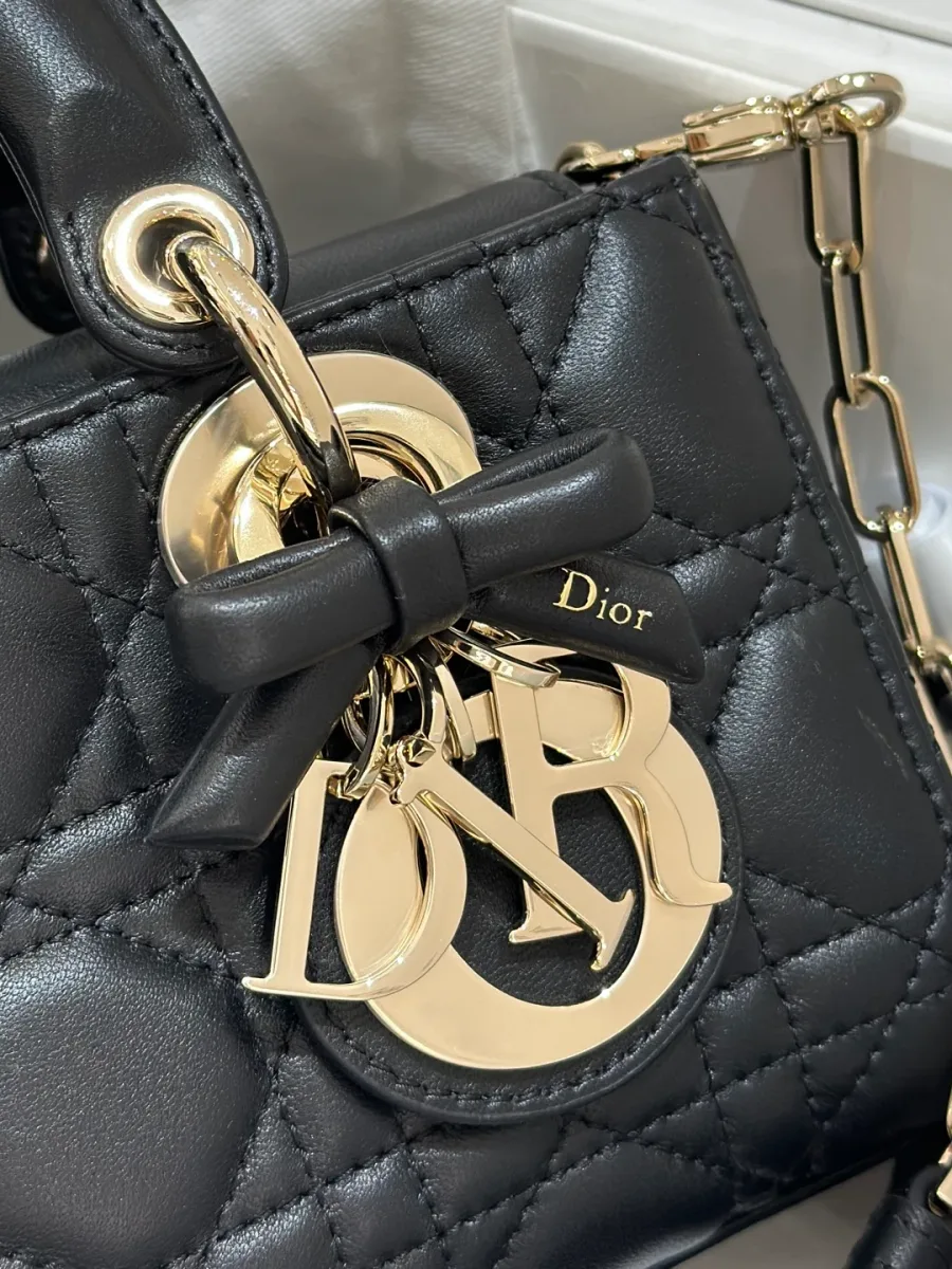 Крупный план золотистой подвески DIOR с черным кожаным бантом