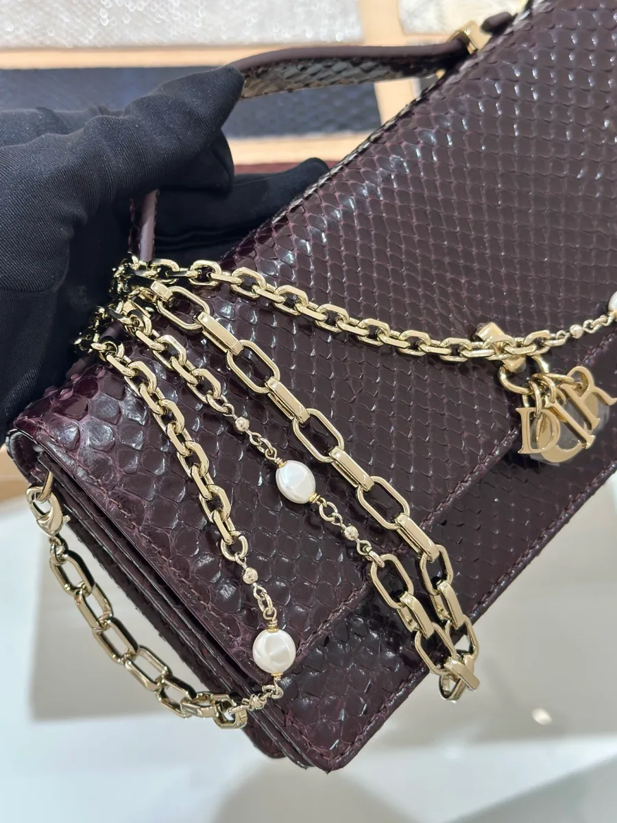 Крупный план золотистой цепочки с жемчужинами и подвески DIOR на бордовом клатче