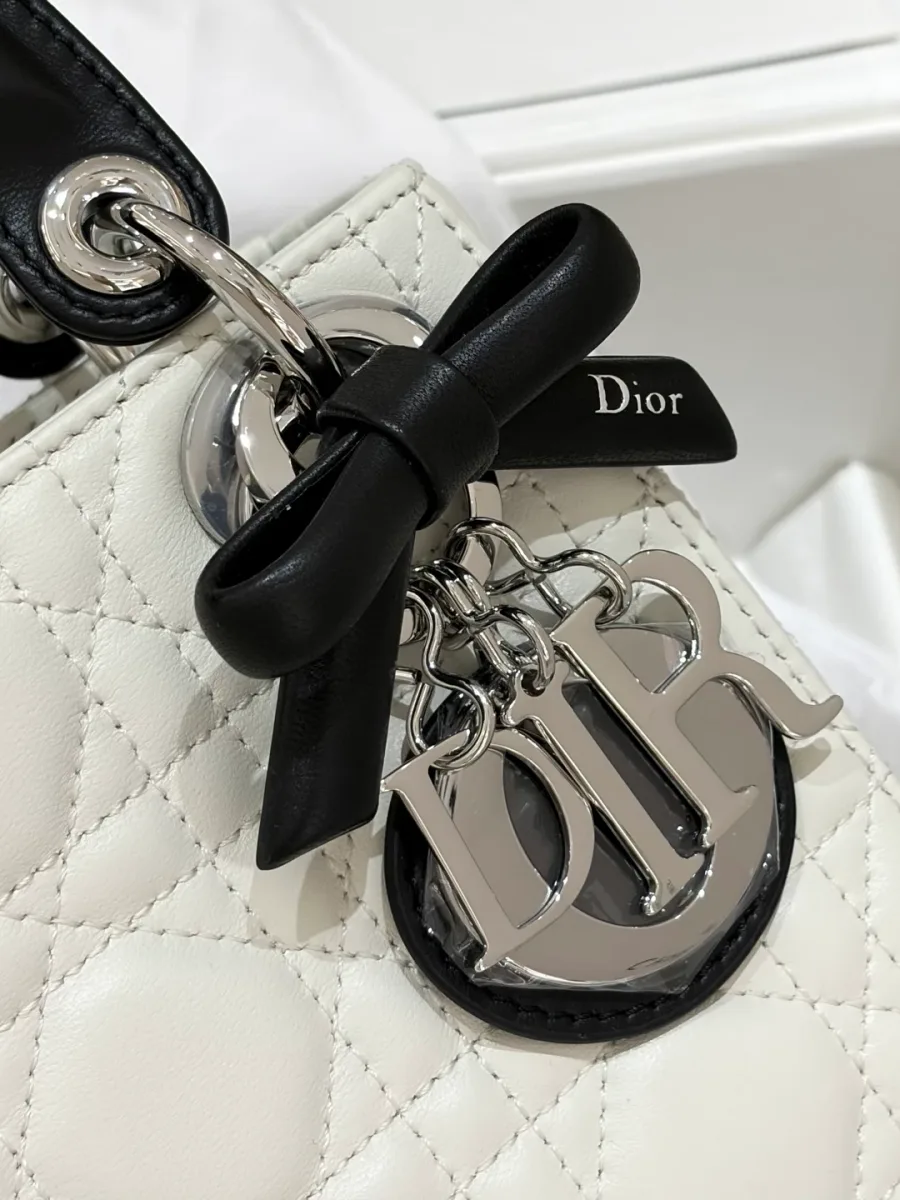 Крупный план серебристой подвески DIOR и черного кожаного банта на сумке