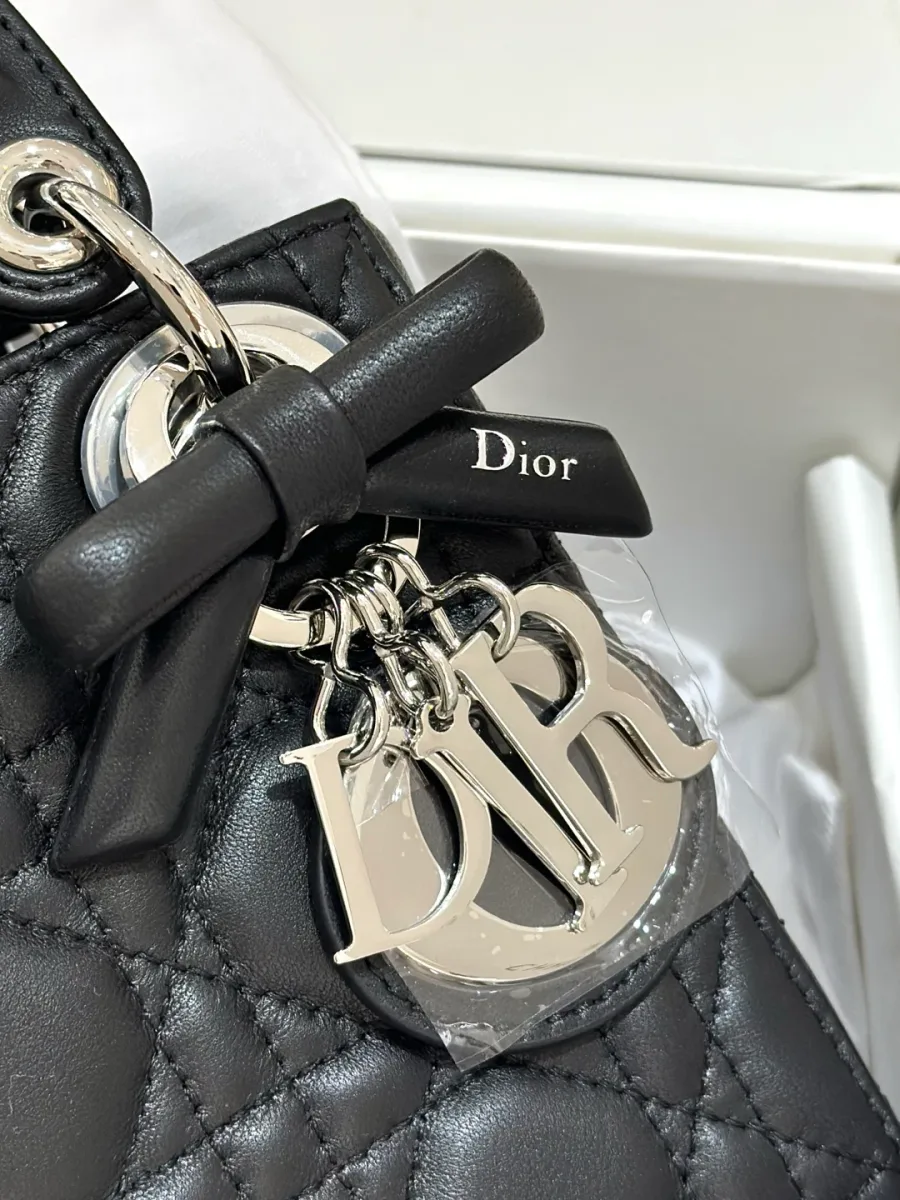 Крупный план серебристой подвески DIOR и кожаного банта на сумке