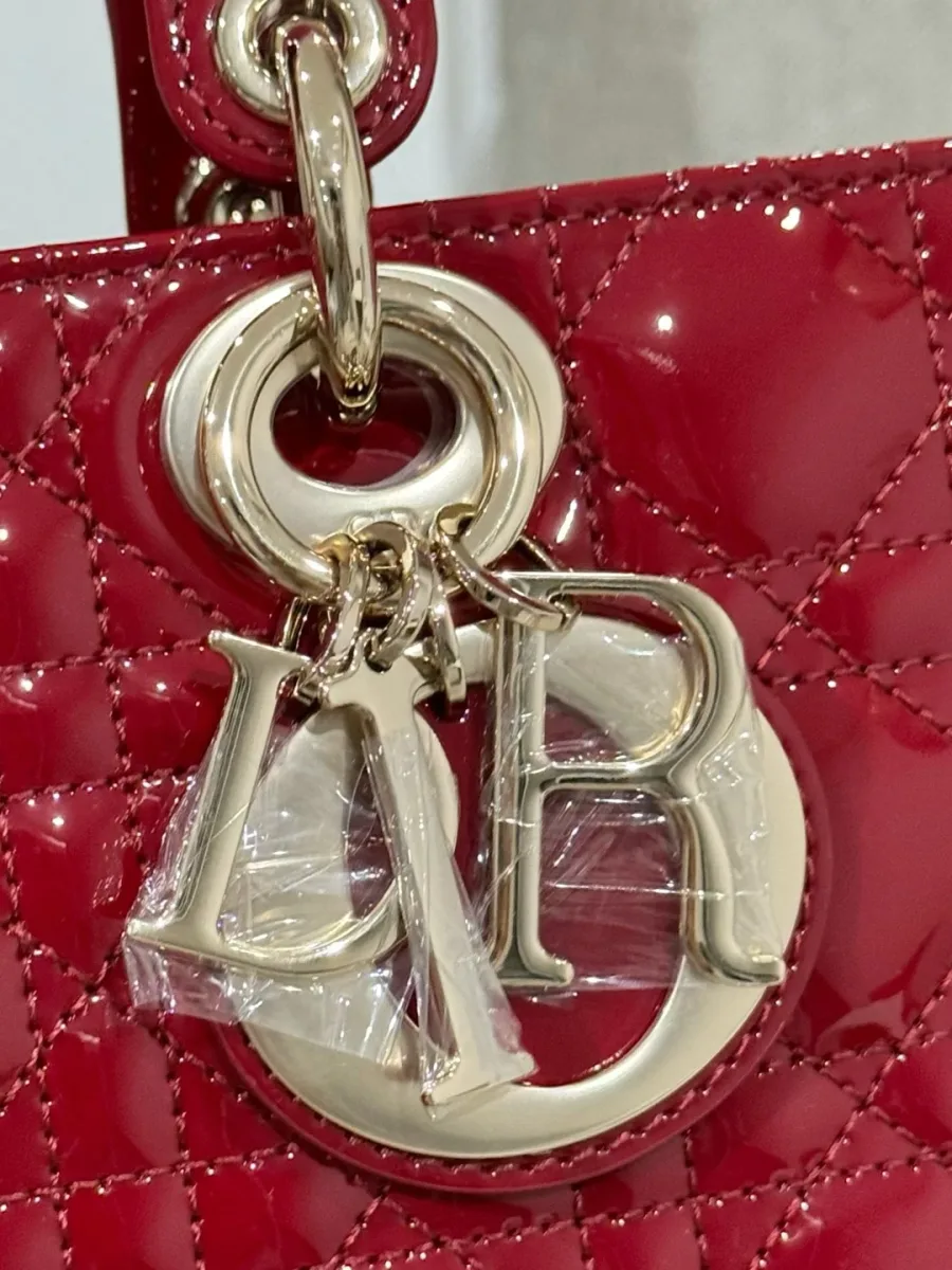 Крупный план золотистой подвески-шарма DIOR на бордовой лакированной коже с узором Cannage