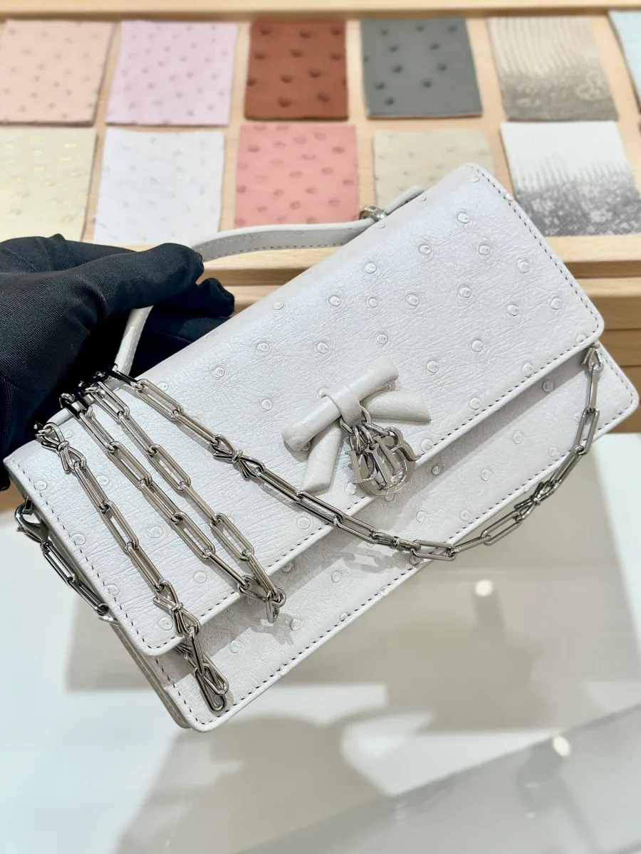 Белый клатч Dior Jolie WOC из кожи страуса с серебристой цепочкой, вид спереди в руке