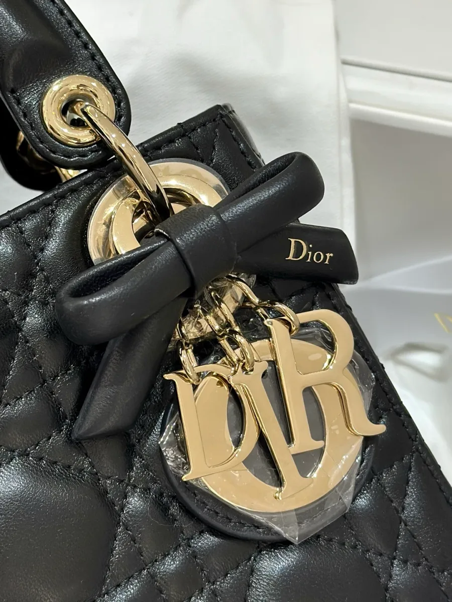 Крупный план золотистой подвески DIOR с черным кожаным бантом на сумке