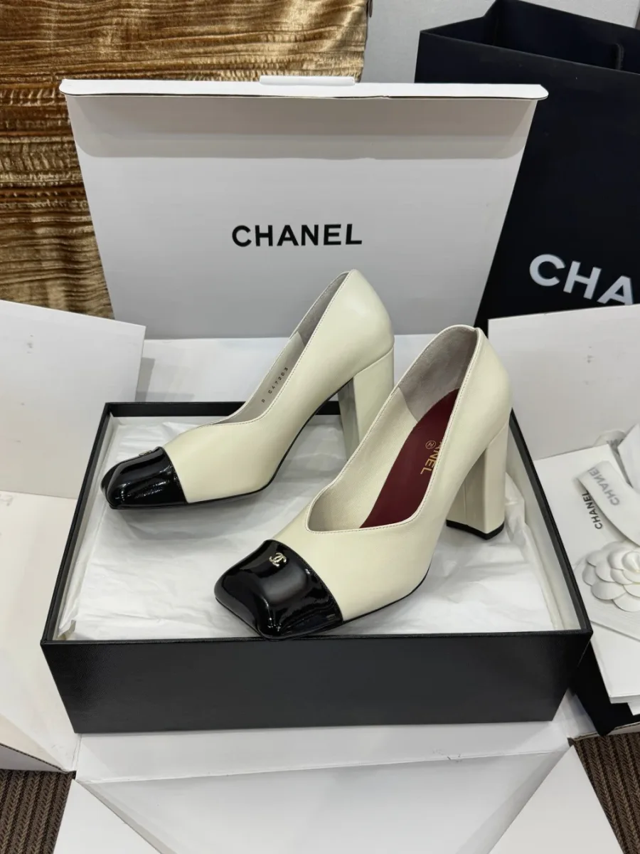 Пара бежевых туфель Chanel с чёрным мыском и логотипом CC, вид сбоку в коробке