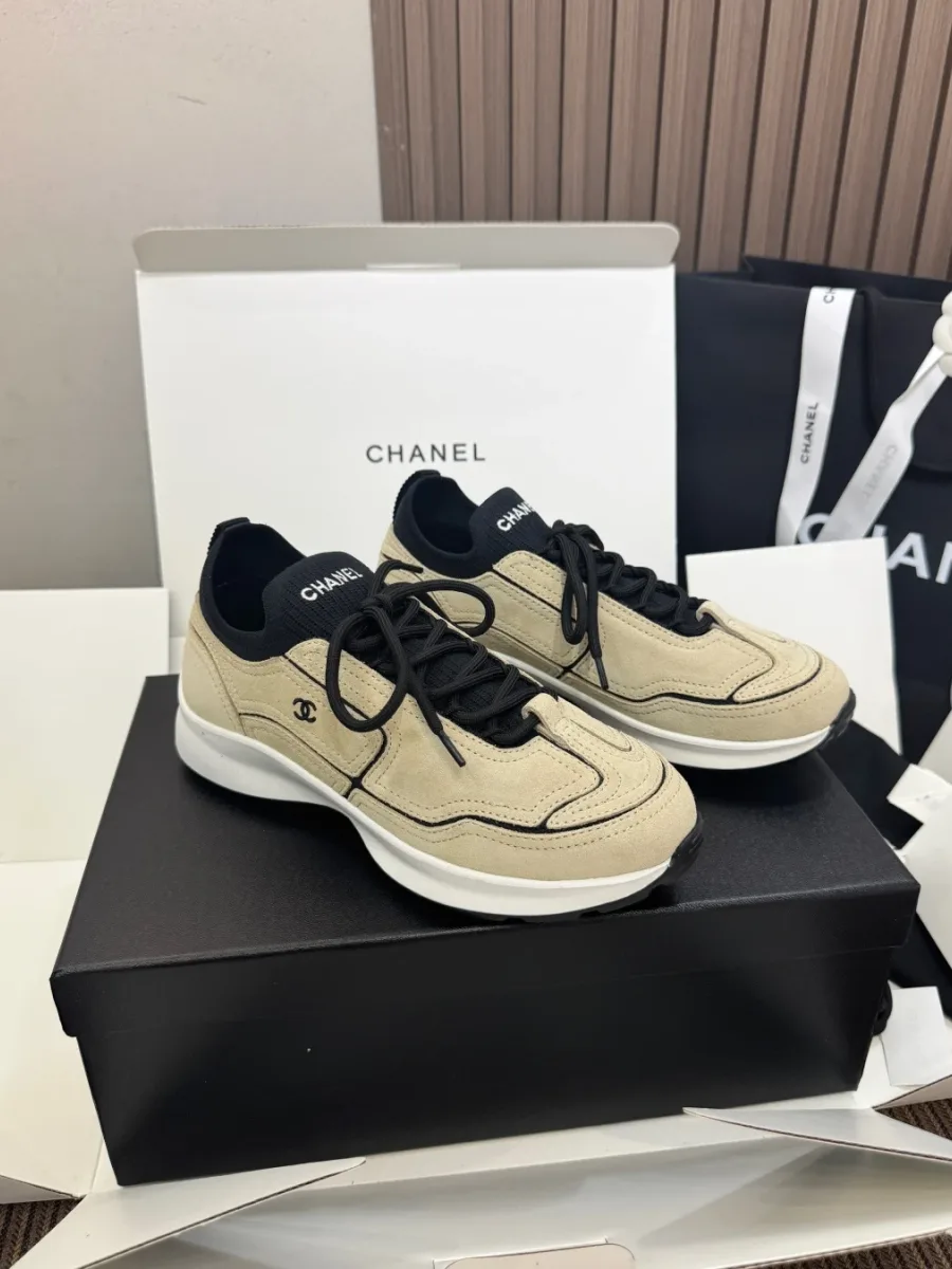 Пара бежевых кроссовок Chanel с чёрными деталями на коробке, ракурс три четверти