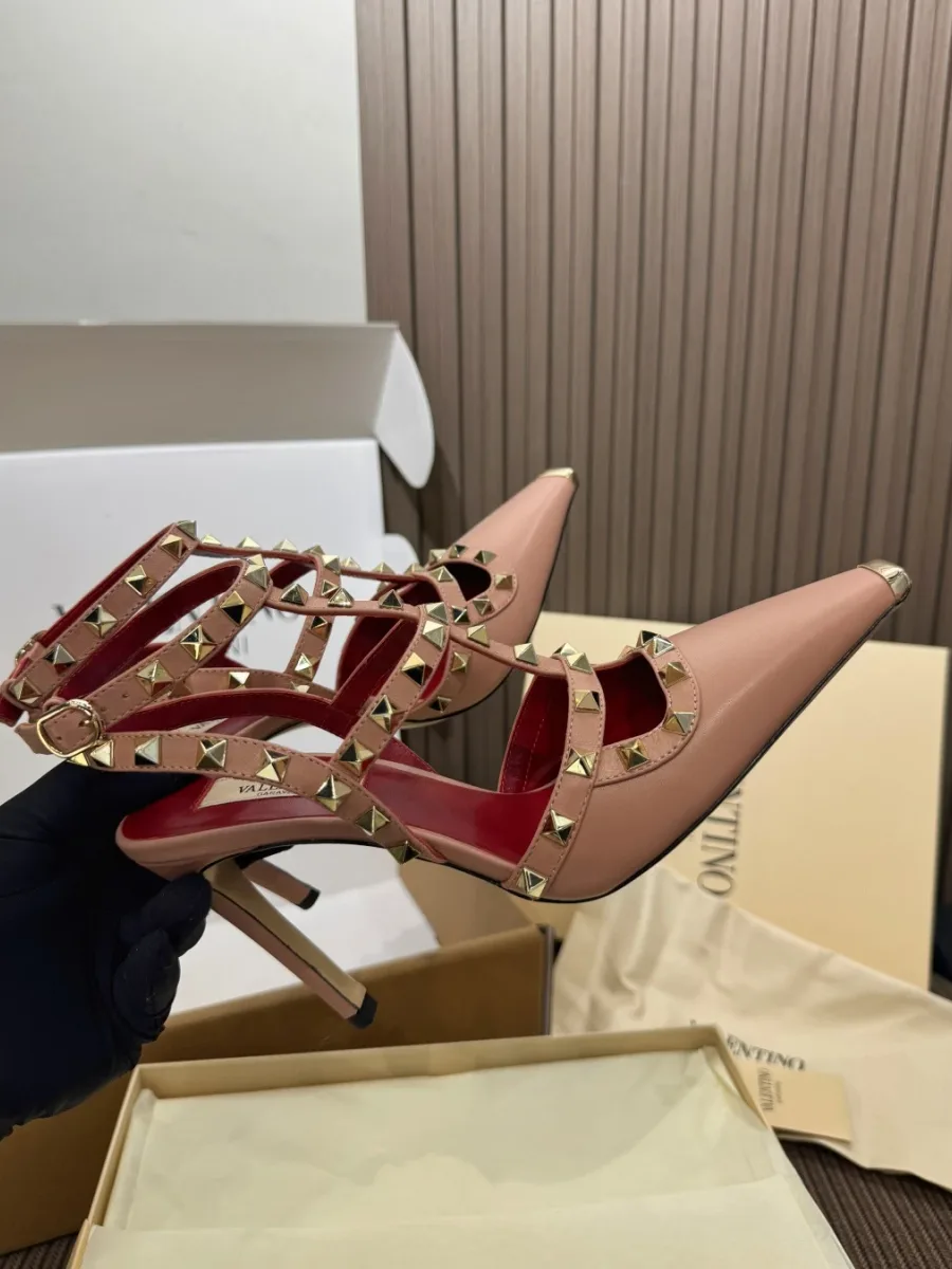 Демонстрация пары босоножек с шипами Rockstud в руке на фоне коробки