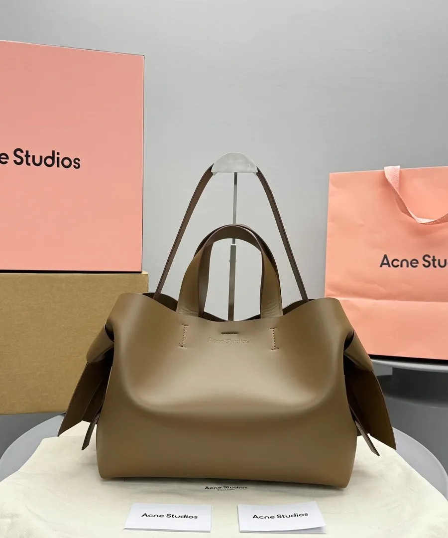 Коричневая кожаная сумка с узлами по бокам, вид спереди рядом с фирменной упаковкой