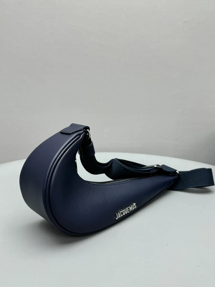 Синяя сумка в форме swoosh, общий вид сбоку на светлой поверхности